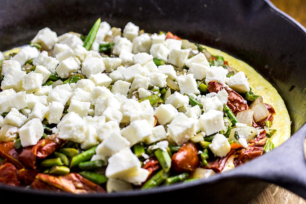 Adding Queso Fresco Cheese to an Omelet in a Cast Iron Skillet