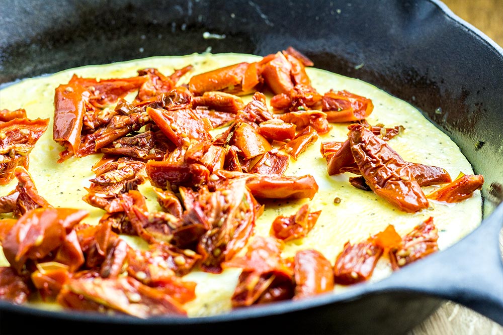 Adding Sun Dried Tomatoes to an Omelet in a Cast Iron Skillet
